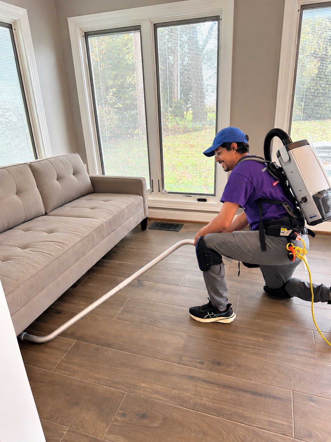 A Cleaning Cardinals team member vacuuming under a sofa with a backpack vacuum after a renovation