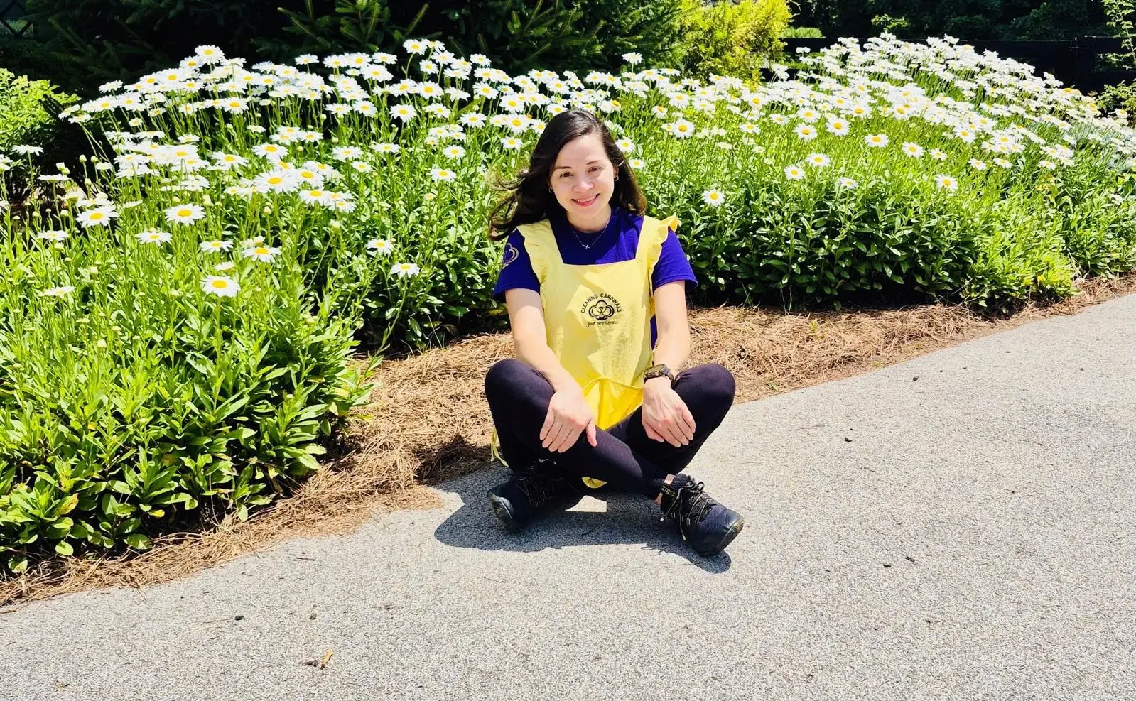 A smiling Cleaning Cardinals team member in her yellow apron sitting among daisies