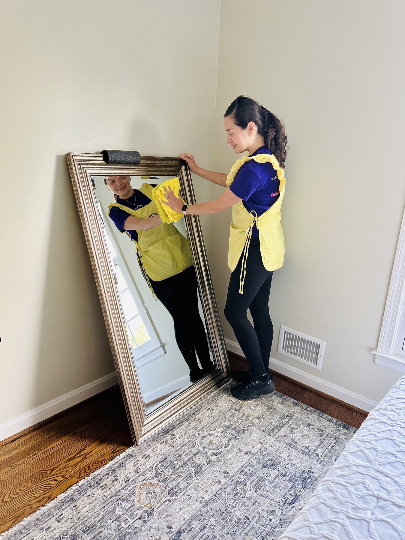 A Cleaning Cardinals team member wiping a full-length mirror until it is streak free