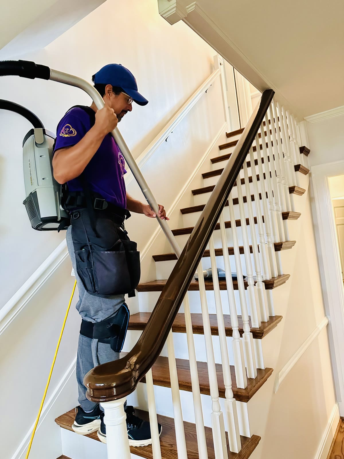 A Cleaning Cardinals team member carrying a backpack vacuum up a staircase