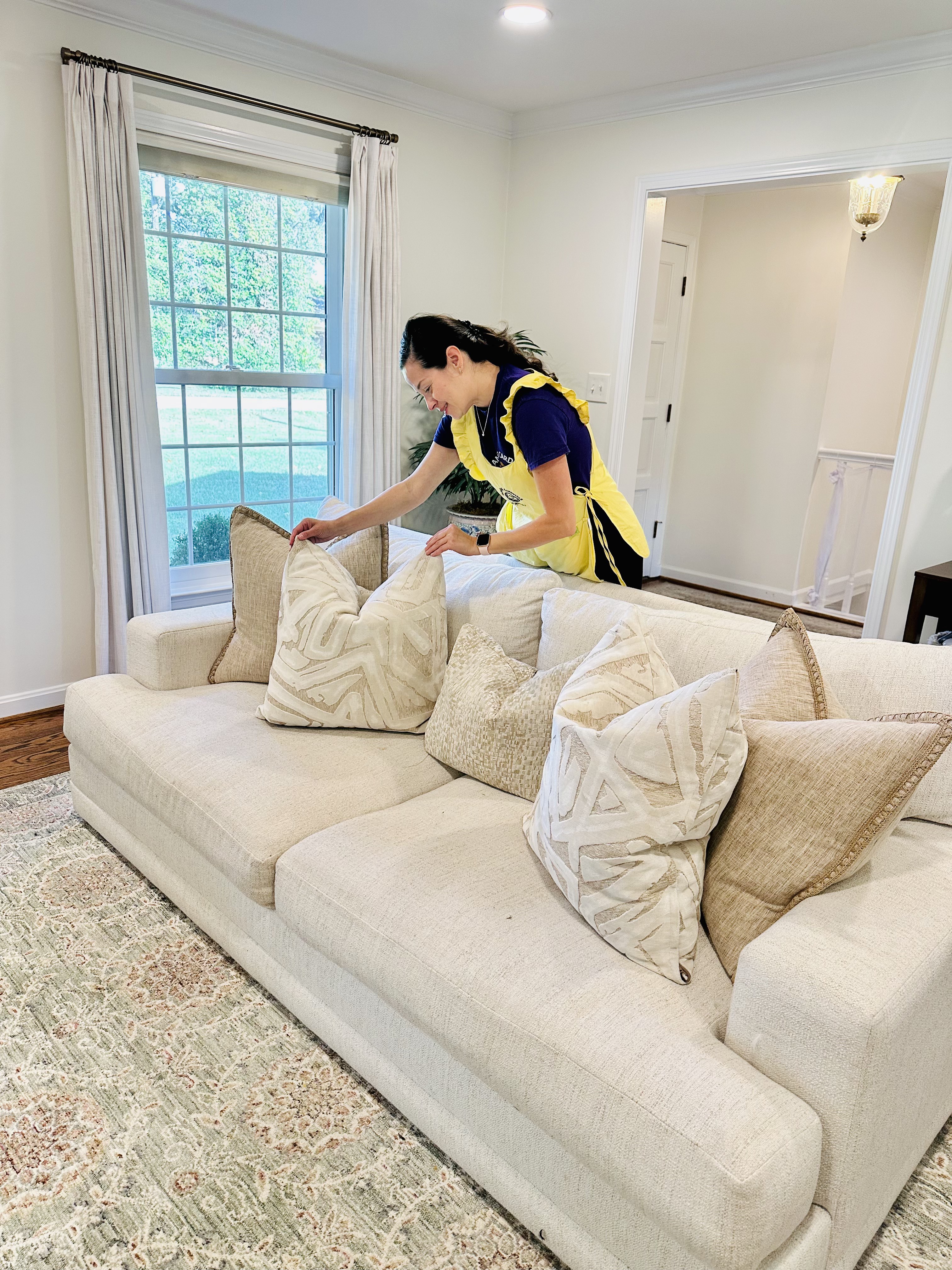 A smiling Cleaning Cardinals team member arranging pillows on a cream sofa